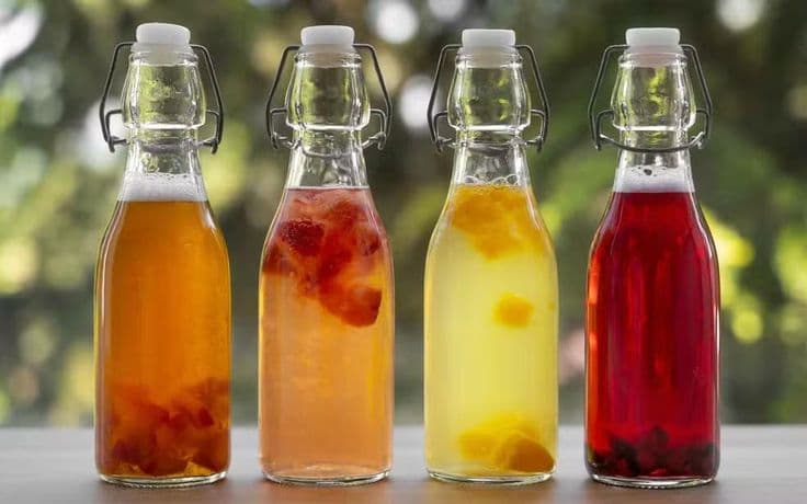 Quatre bouteilles de vins de fruits en fermentation, avec des morceaux de fruits